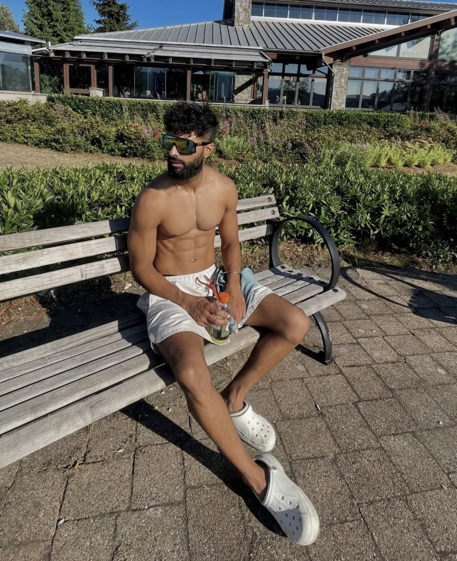 Harry Johal seated on a park bench in summer, sunglasses and shorts.